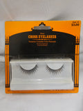 Packaged pair of silver cross eyelashes in a white plastic tray on an orange and black retail card, photographed against a white fabric background.