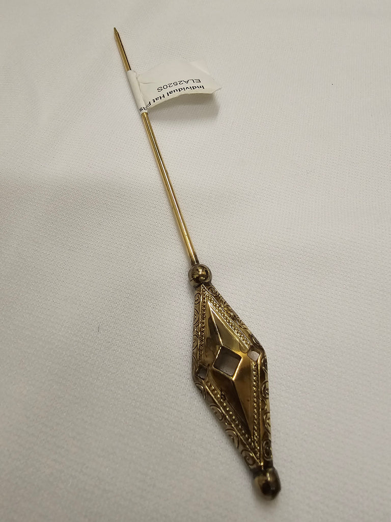 An antique Victorian hat pin made of gold-toned metal, featuring a faceted diamond-shaped pendant with engraved details and a long pin stem. A small white paper tag is attached near the top.