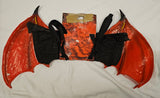 A pair of red and black bat wings laid flat on a white fabric background, with a matching red and black fabric wing-like accessory and a crumpled orange paper piece behind them.