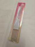 A white plastic comb with four metal tail pins, packaged in a pink and beige cardboard sleeve on a light gray fabric background.