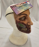 A severed zombie face mask displayed on a white mannequin head, with its retail packaging card attached across the forehead. The package reads 'FRACTURED Fun Face Fx' and shows the brand 'AMT'.