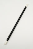 A black cylindrical rod or stick with white plastic end caps, photographed diagonally on a white textured fabric background.