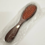 A wooden hairbrush with reddish-brown bristles and white dot details, wrapped in clear plastic packaging on a light gray background.