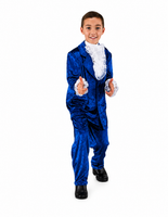 A young boy modeling a royal blue velvet costume suit with white ruffled lace details on the collar and cuffs, paired with black shoes, against a solid white background.