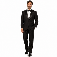 A man modeling a classic black tuxedo with satin peak lapels, a white dress shirt, a black bow tie, and black dress shoes against a plain white background.