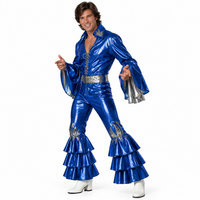 A man modeling a shiny royal blue Elvis-style jumpsuit costume with silver trim, flared bell sleeves, and tiered ruffle hems, paired with white boots against a plain white background.