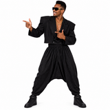 A man modeling a black harem pants costume set consisting of a cropped blazer jacket, matching baggy pants, and black sneakers, posed against a solid white background.