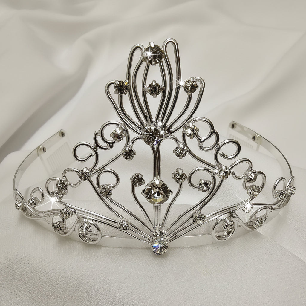 An ornate silver tiara crown with intricate filigree wirework and clear rhinestones, displayed on a white fabric background.